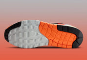 Sneakers Nike Air Max 1 Patta Waves Hyper Crimson Pure Platinum en mesh gris et cuir avec garde-boue ondulé orange et unité Air visible.