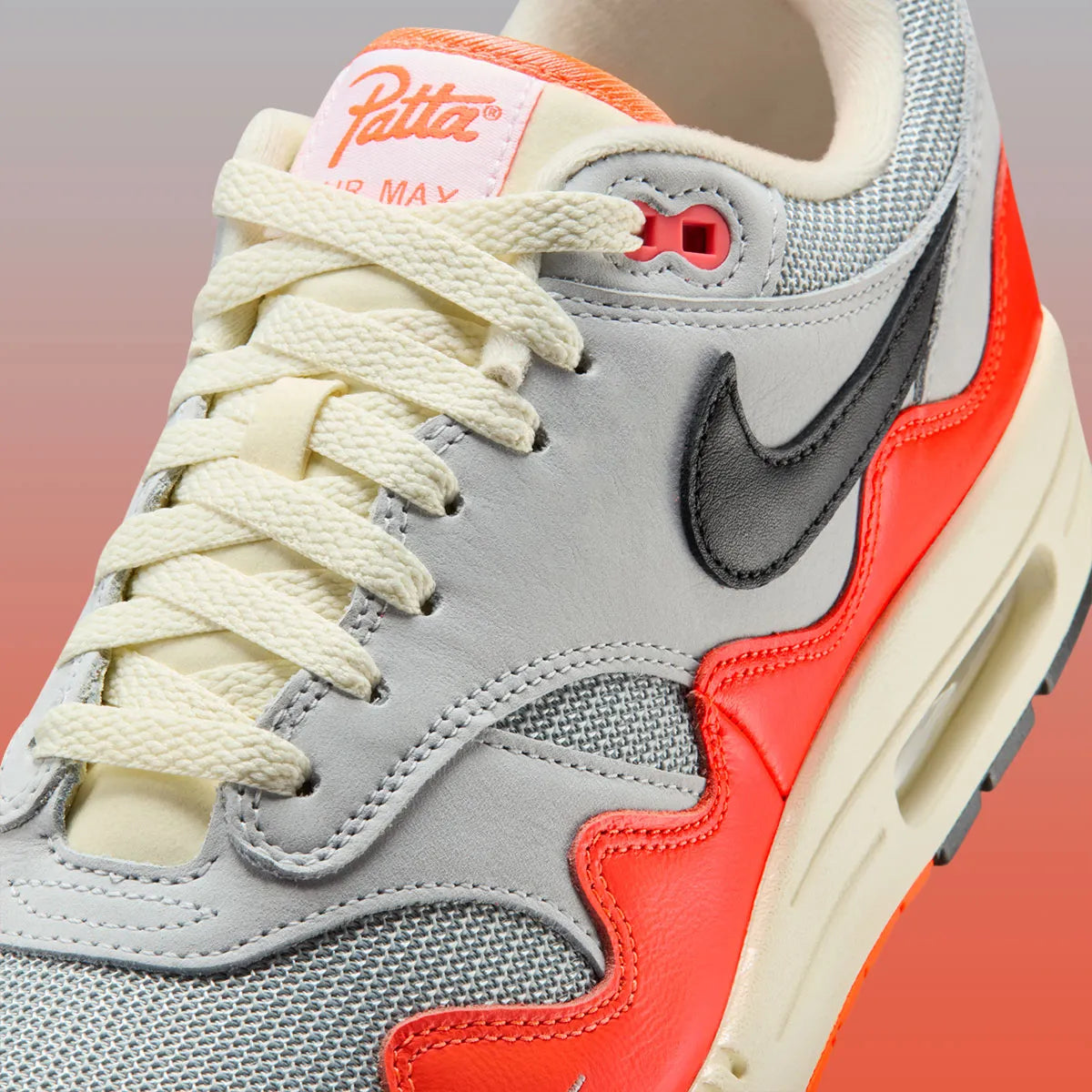 Sneakers Nike Air Max 1 Patta Waves Hyper Crimson Pure Platinum en mesh gris et cuir avec garde-boue ondulé orange et unité Air visible.