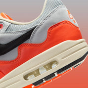 Sneakers Nike Air Max 1 Patta Waves Hyper Crimson Pure Platinum en mesh gris et cuir avec garde-boue ondulé orange et unité Air visible.