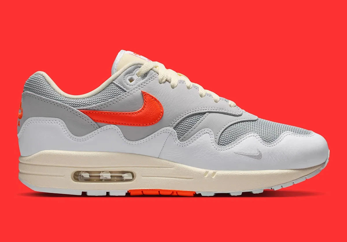 Sneakers Nike Air Max 1 Patta Waves White Hyper Crimson en mesh blanc avec mudguard ondulé orange et unité Air visible vue de profil. 
