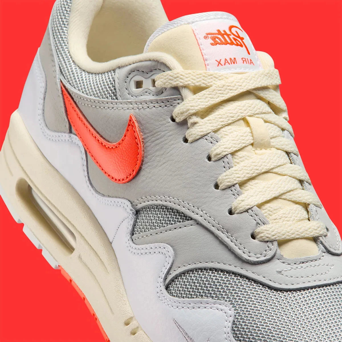 Vue sur les détails latéraux de la Sneakers Nike Air Max 1 Patta Waves White Hyper Crimson en mesh blanc avec mudguard ondulé orange et unité Air visible.