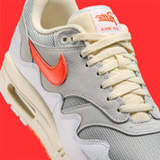 Vue sur les détails latéraux de la Sneakers Nike Air Max 1 Patta Waves White Hyper Crimson en mesh blanc avec mudguard ondulé orange et unité Air visible.