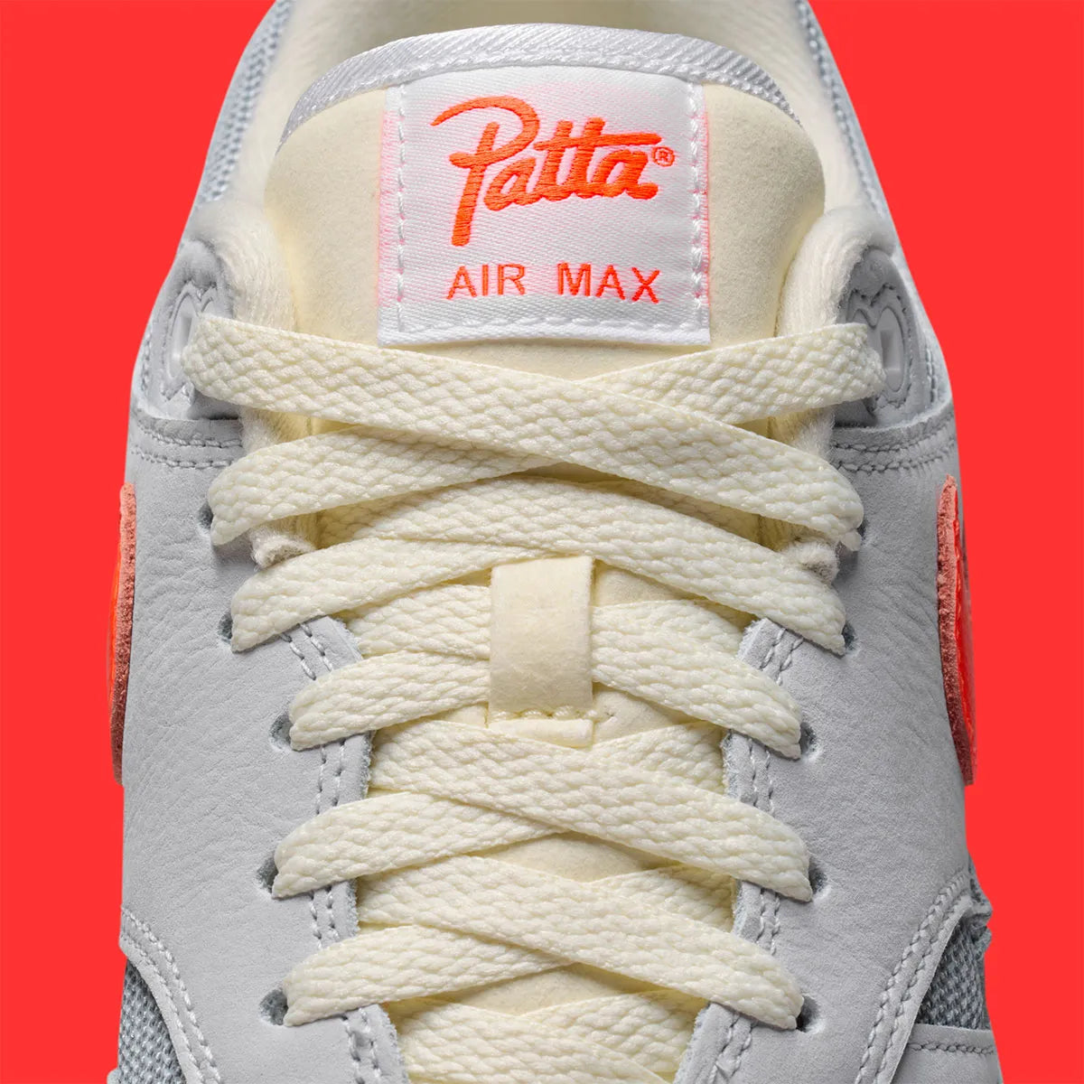 Vue détaillée sur la languette de la Sneakers Nike Air Max 1 Patta Waves White Hyper Crimson en mesh blanc avec mudguard ondulé orange et unité Air visible.
