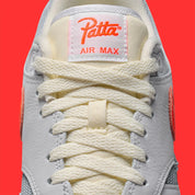 Vue détaillée sur la languette de la Sneakers Nike Air Max 1 Patta Waves White Hyper Crimson en mesh blanc avec mudguard ondulé orange et unité Air visible.